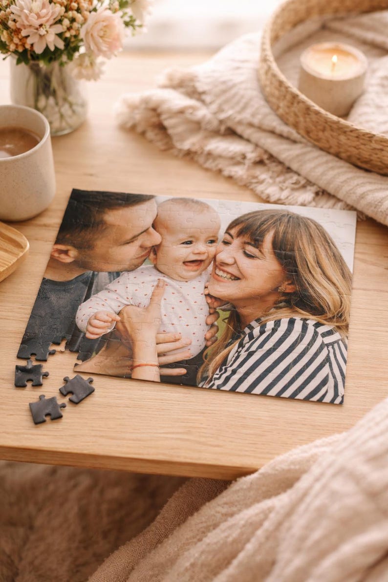 May include: A personalized photo puzzle featuring a family portrait. The image shows a smiling baby being kissed by two adults. Several puzzle pieces are separate from the assembled image, resting on a wooden surface.