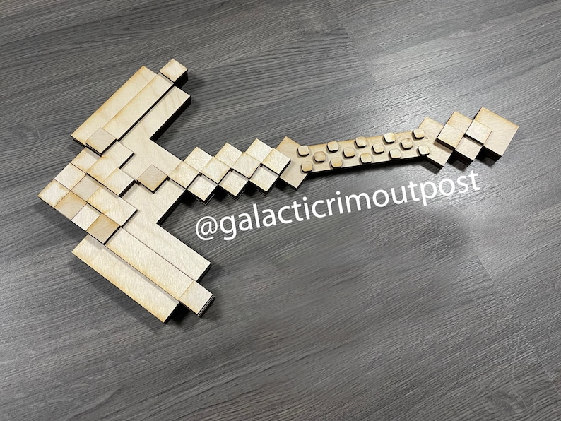 K&ouml;nnte beinhalten: Ein pixeliger Hammer aus Holz, wahrscheinlich f&uuml;r dekorative Zwecke. Der Hammer besteht aus hellem Holz und hat einen Griff mit quadratischen Aussparungen. Der Text "@galacticrimoutpost" ist auf der Oberfl&auml;che sichtbar.