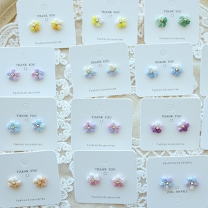 Op de afbeelding: Assortiment van 10 paar kleine bloemvormige oorbellen op witte kaartjes met de tekst "Bedankt" en "Modeaccessoires". De oorbellen zijn in verschillende pastelkleuren, waaronder roze, blauw, geel en groen.