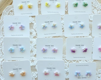 May include: Assortment of 10 pairs of small flower-shaped earrings on white cards with the text "Thank You" and "Fashion Accessories". The earrings are in various pastel colours, including pink, blue, yellow, and green.