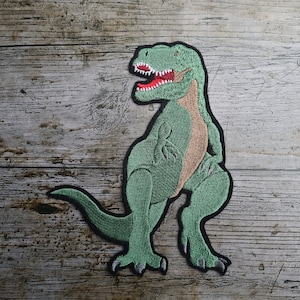 May include: Green embroidered iron-on patch of a dinosaur with a red mouth and brown accents.