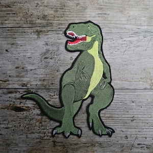 May include: Green embroidered iron-on patch of a Tyrannosaurus Rex dinosaur with a red mouth and yellow accents.