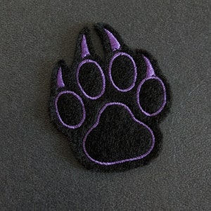 Könnte beinhalten: Lilafarbener gestickter Pfotenabdruck-Patch auf schwarzem Hintergrund.