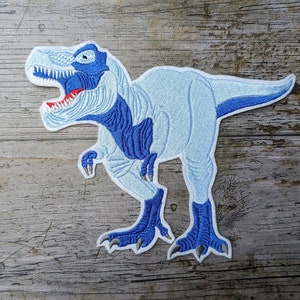 May include: A blue and white embroidered iron-on patch of a Tyrannosaurus Rex dinosaur.