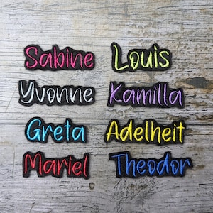 Può includere: Otto toppe con nomi ricamate da stirare in diversi colori. I nomi sono: Sabine, Louis, Yvonne, Kamilla, Greta, Adelheit, Mariel e Theodor.