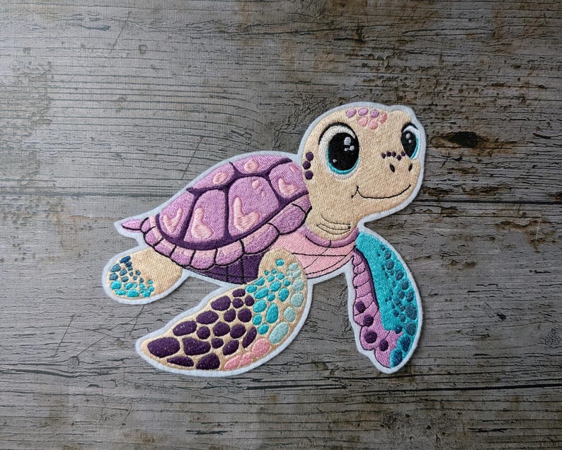 May include: Embroidered patch of a cartoon sea turtle. The turtle has a purple shell, pink and blue flippers, and a beige face with large black eyes. The patch has a white border and is set against a wooden background.