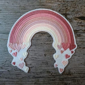 Peut inclure: Écusson arc-en-ciel brodé dans les tons roses, avec une bordure blanche. Le motif arc-en-ciel présente plusieurs couches de couleurs et est orné d'accents en forme de cœur aux extrémités. Un article décoratif pour vêtements ou accessoires.