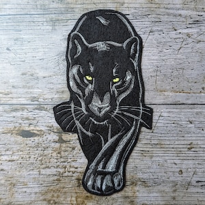 Könnte beinhalten: Schwarzer gestickter Bügel-Patch mit einer Panther-Darstellung und gelben Augen. Der Panther blickt nach vorne, der Mund ist geschlossen und die Pfoten sind sichtbar.