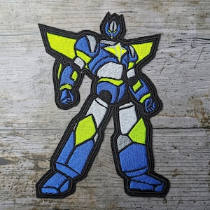Puede incluir: Parche bordado de un robot azul y amarillo con una estrella en el pecho. El robot tiene un contorno negro y está de pie con los brazos a los lados.