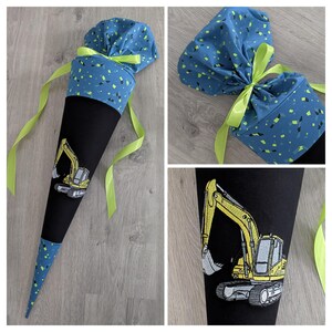 Könnte beinhalten: Schultüte in Schwarz und Blau mit gelbem Bagger-Design. Die Tüte hat einen blauen Stoffaufsatz mit grünen und gelben Akzenten, der mit einem grünen Band gebunden ist.