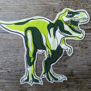 May include: Green and white embroidered iron-on patch of a Tyrannosaurus Rex dinosaur with an open mouth.
