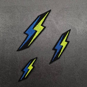 May include: Three embroidered iron-on patches in the shape of a lightning bolt. The patches are black with a yellow and blue lightning bolt design.