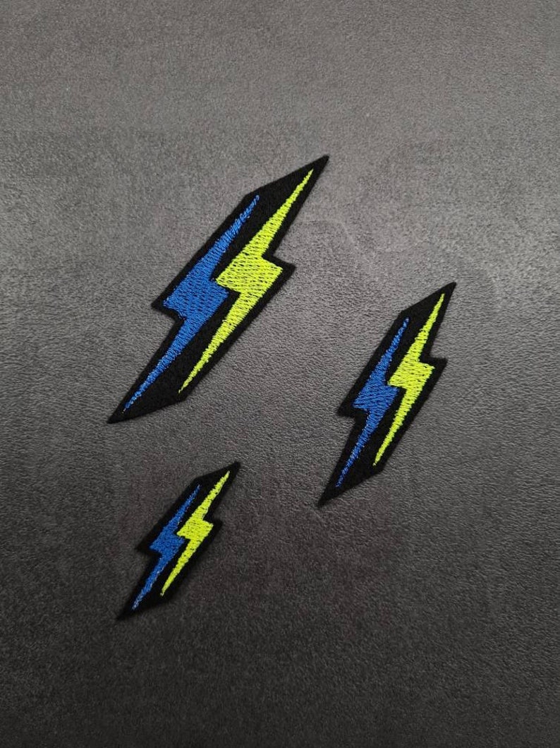 May include: Three embroidered iron-on patches in the shape of a lightning bolt. The patches are black with a yellow and blue lightning bolt design.