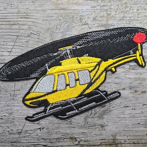 Könnte beinhalten: Gelber Hubschrauber-Stick mit schwarzen Rotorblättern und rotem Hecklicht. Der Hubschrauber ist mit grauen Landekufen und Fenstern detailliert.