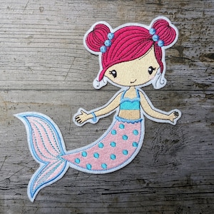 May include: Embroidered iron-on patch of a pink and blue mermaid with pink hair and blue eyes. The mermaid is wearing a blue top and a pink skirt with blue polka dots.