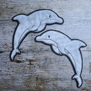 May include: Two gray felt dolphin shapes with black outlines, on a wood background.
