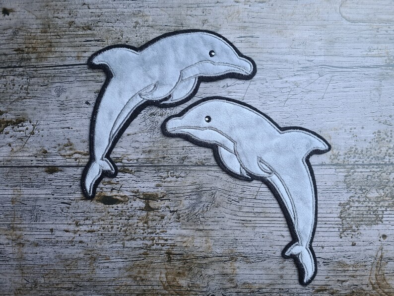 May include: Two gray felt dolphin shapes with black outlines, on a wood background.