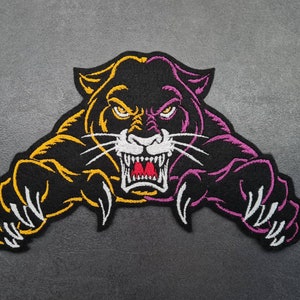 May include: Embroidered patch depicting a snarling panther with a fierce expression. The panther is black with yellow and purple accents, sharp white teeth, and extended claws. The patch is designed to be sewn or ironed onto fabric.