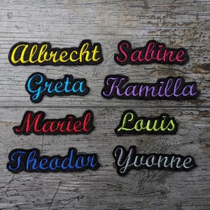 May include: Eight embroidered name tags with different names in various colors. The names are Albrecht, Sabine, Greta, Kamilla, Mariel, Louis, Theador, and Yvonne.