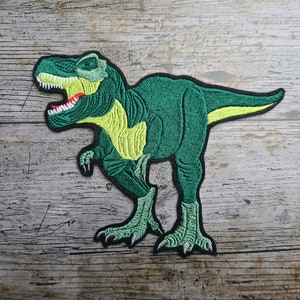 Puede incluir: Parche verde bordado para planchar de un dinosaurio Tyrannosaurus Rex con vientre amarillo y dientes rojos.
