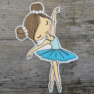 Könnte beinhalten: Gestickter Bügel-Aufnäher einer Ballerina mit braunen Haaren, einem hellblauen Tutu und weißen Schuhen. Die Ballerina lächelt und hat die Arme in die Luft gestreckt.