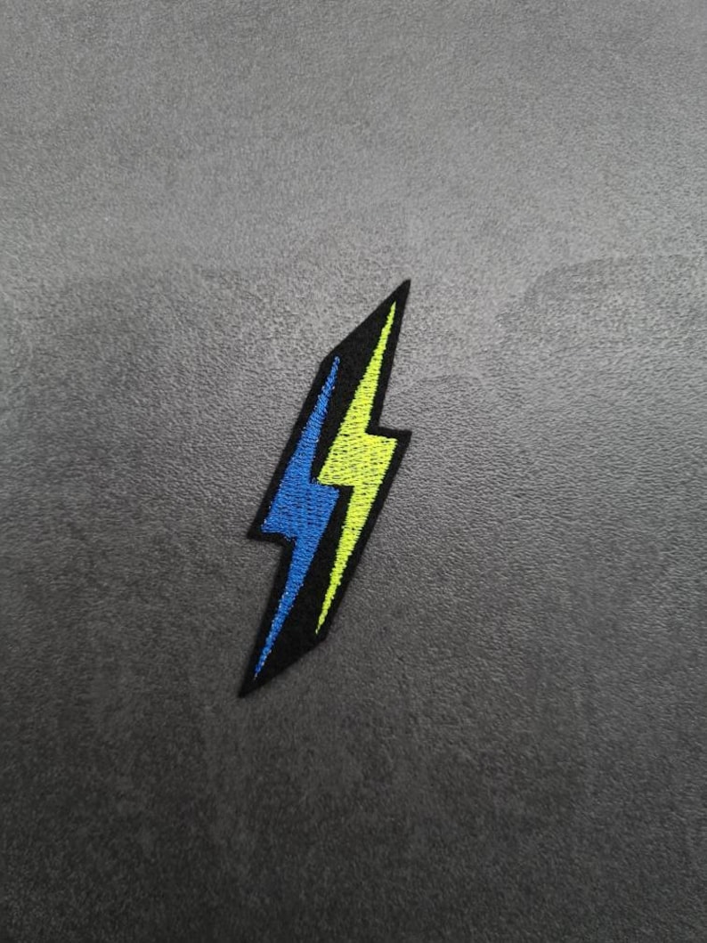 May include: A yellow and blue lightning bolt embroidered patch. The patch is black with a yellow outline and a blue lightning bolt inside.