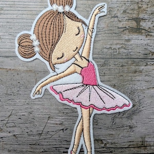 Könnte beinhalten: Gestickter Aufnäher mit einer Cartoon-Ballerina in einer anmutigen Pose. Die Ballerina trägt einen rosa Body und Tutu mit passenden Spitzenschuhen. Ihr Haar ist zu einem Dutt mit einem weißen Blumenhaarschmuck hochgesteckt. Der Aufnäher hat einen weißen Rand.