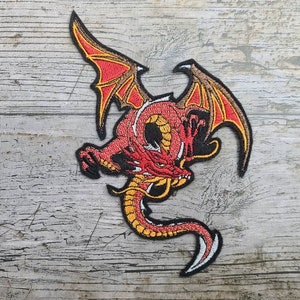 Puede incluir: Parche de hierro bordado en rojo y dorado de un dragón con las alas extendidas.