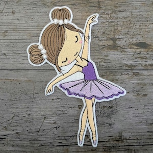 May include: Iron-on patch featuring an embroidered ballerina with brown hair, a purple leotard, and a lavender tutu.