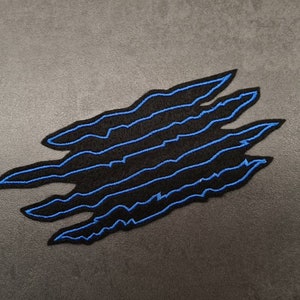 May include: Black and blue embroidered patch shaped like a claw mark.