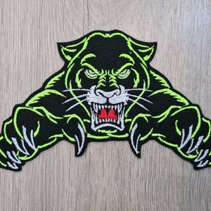 May include: Green and black embroidered patch of a snarling panther with white claws and teeth. The panther is facing forward with its mouth open and its claws extended.