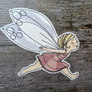 Puede incluir: Parche bordado de un hada con alas rosas y un vestido rosa volando con los brazos extendidos. El hada tiene el pelo rubio y una cara sonriente.