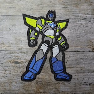Puede incluir: Parche bordado para planchar con un robot en un esquema de colores azul, gris, blanco y amarillo. El robot tiene una cabeza en forma de estrella y está de pie con los brazos extendidos.