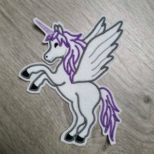 Peut inclure: Patch en feutre blanc représentant une licorne avec une crinière et une queue violettes, et des ailes noires. La licorne a une corne violette et des yeux noirs.