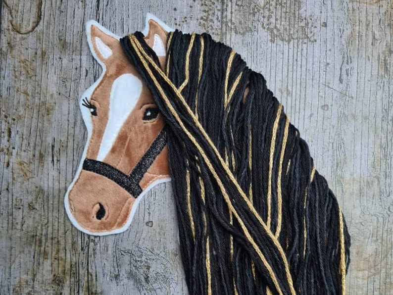 May include: A brown horse head applique with a black and gold yarn mane. The horse has a black leather bridle with glitter accents.