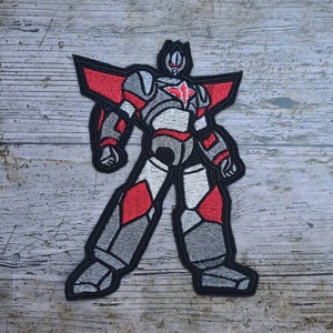 Può includere: Toppa ricamata da stirare con un robot grigio e rosso con una stella sul petto. Il robot ha un contorno nero e sta in piedi con le gambe divaricate.