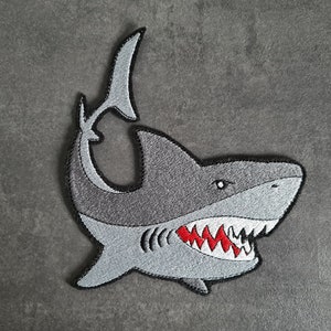 May include: A gray embroidered shark patch with a red open mouth and sharp teeth.