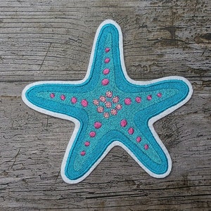 May include: A blue and pink embroidered starfish patch. The starfish is outlined in white and has a pink center with white dots.