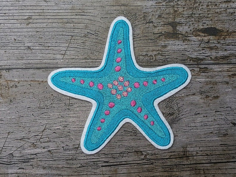 May include: A blue and pink embroidered starfish patch. The starfish is outlined in white and has a pink center with white dots.