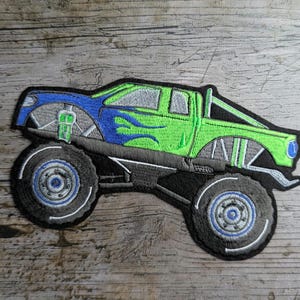May include: Green and blue monster truck applique with flames on the side. The truck has large black tires with silver rims.