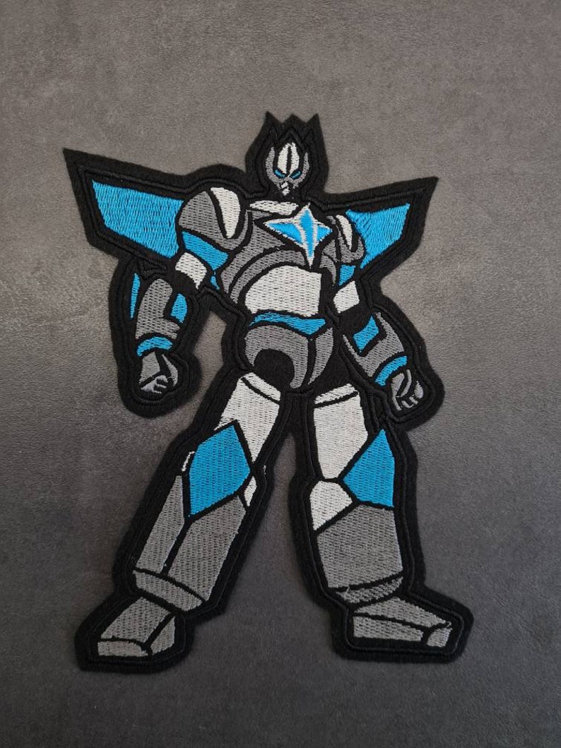 May include: A blue and gray embroidered patch of a robot with a star on its chest.