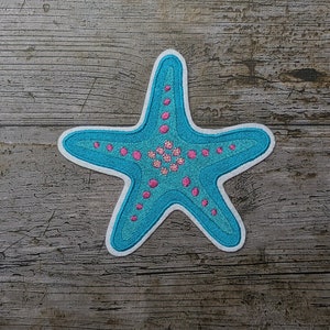 May include: A blue and pink embroidered starfish patch. The starfish has a white outline and is decorated with pink dots and flowers.