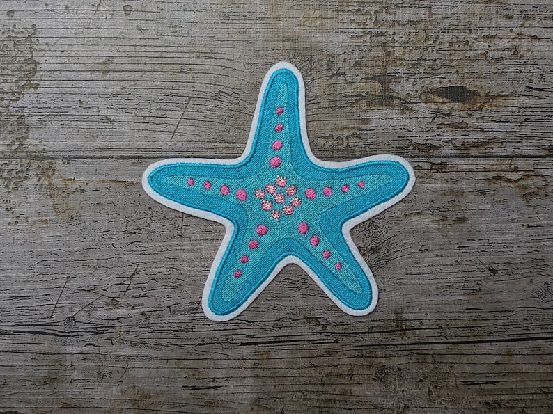 May include: A blue and pink embroidered starfish patch. The starfish has a white outline and is decorated with pink dots and flowers.