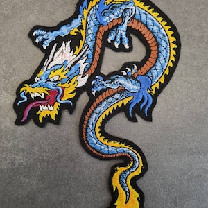 Könnte beinhalten: Ein gestickter Drachen-Patch in Blau und Gelb mit einem wütenden Ausdruck. Der Drache ist mit seinem Schwanz im Maul zusammengerollt. Der Patch ist perfekt, um Kleidung, Taschen oder anderen Accessoires einen Hauch von asiatisch inspiriertem Stil zu verleihen.