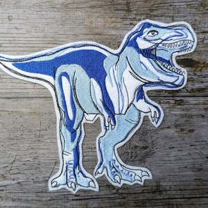 May include: Blue and white embroidered patch of a Tyrannosaurus Rex dinosaur with an open mouth.