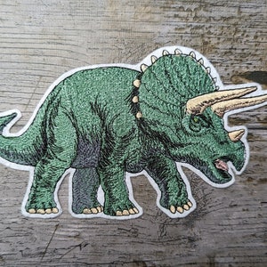 Könnte beinhalten: Grün gestickter Bügel-Patch mit einem Triceratops-Dinosaurier mit weißem Umriss.