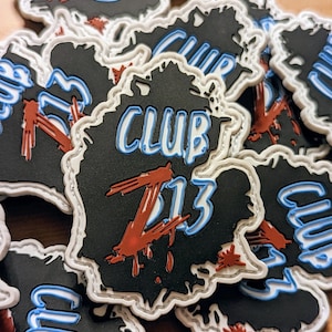 May include: A stack of black and white patches with a red and blue graphic of the text "CLUB Z13" with a dripping red paint effect.