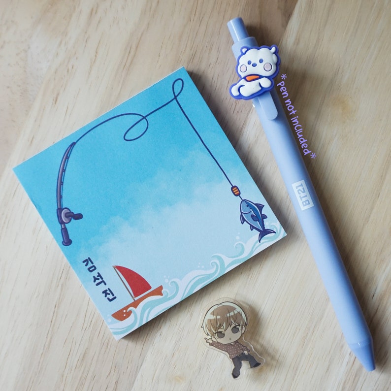 May include: A light blue pen with a white bear design, a blue notepad with a fishing theme, and a small anime character charm. The notepad features a fishing rod, a fish, and a sailboat. The pen has the text "BT21".