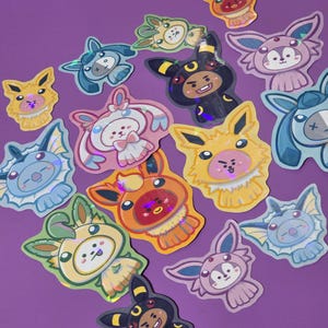 May include: A collection of holographic stickers featuring various cartoon characters dressed in colourful animal-themed costumes. The stickers display diverse creatures in shades of yellow, blue, pink, orange, and black against a purple background.