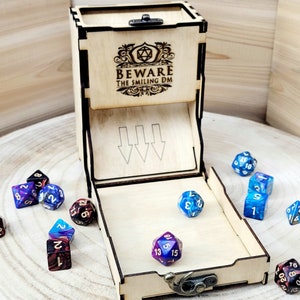 May include: Wooden dice tower with a hinged lid and a compartment for dice. The tower has a laser-engraved design that says "Beware the Smiling DM". The tower is open and there are several colorful dice inside and outside the tower.